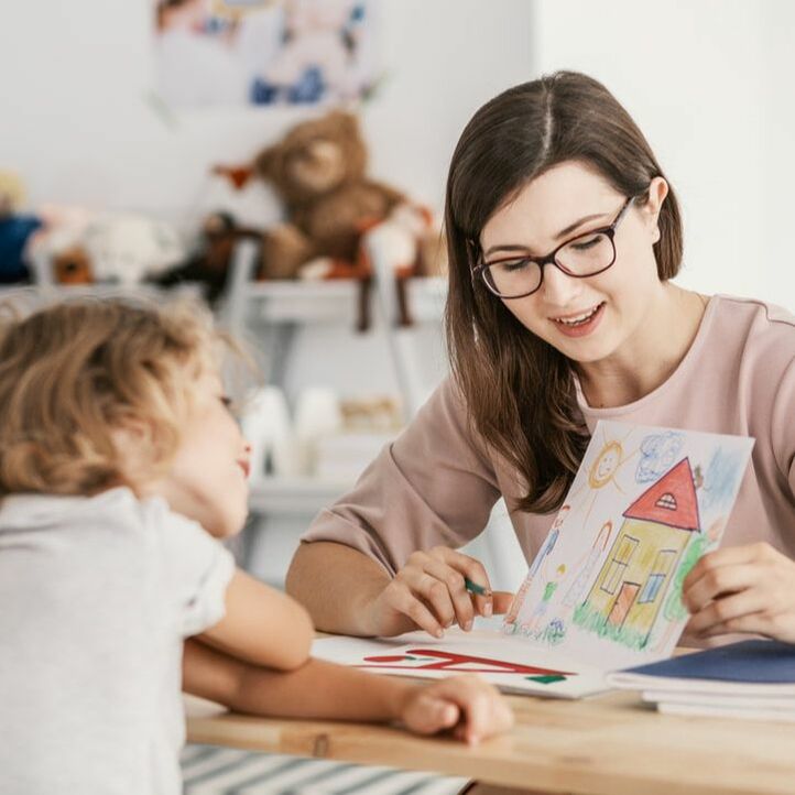Woman with dark hair and glasses holding child's drawing of a house